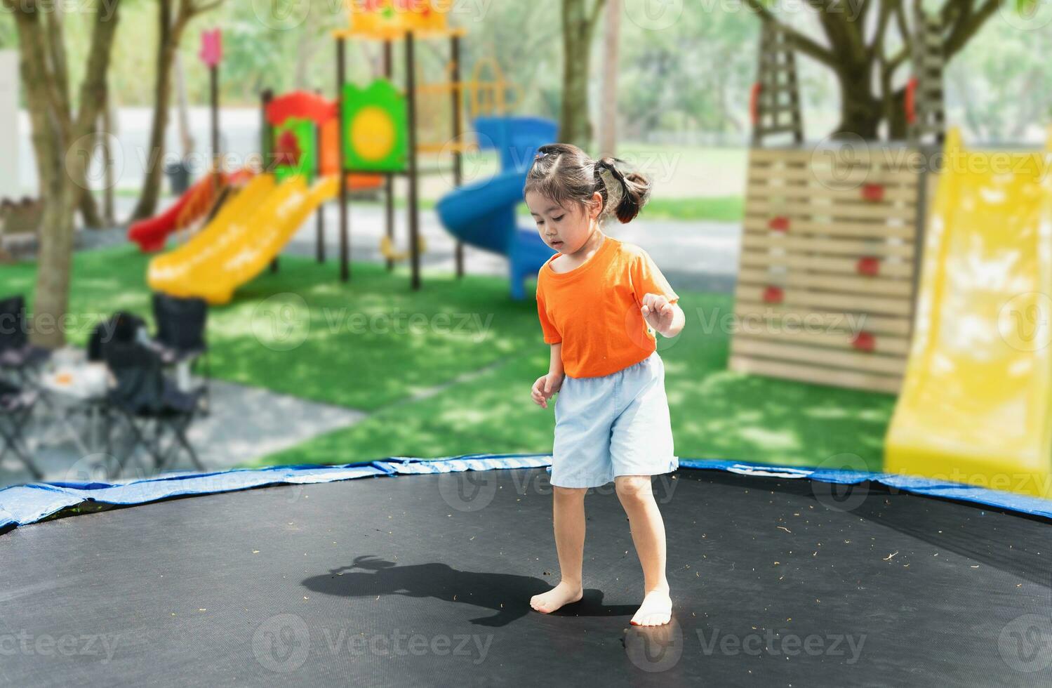 asiatisch Kind Mädchen ist Springen auf Trampolin auf Spielplatz Hintergrund. glücklich Lachen Kind draußen im das Hof auf Sommer- Urlaub. springen hoch auf Trampolin. Aktivität Kinder im das Kindergarten Schule. foto