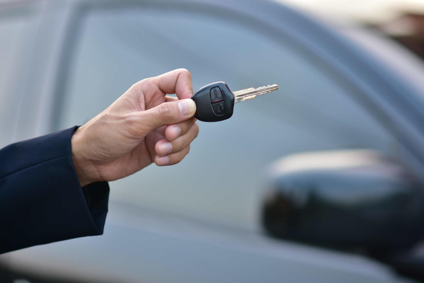 Verkäufer, der den Schlüssel des Autos und des geparkten Autos hält foto