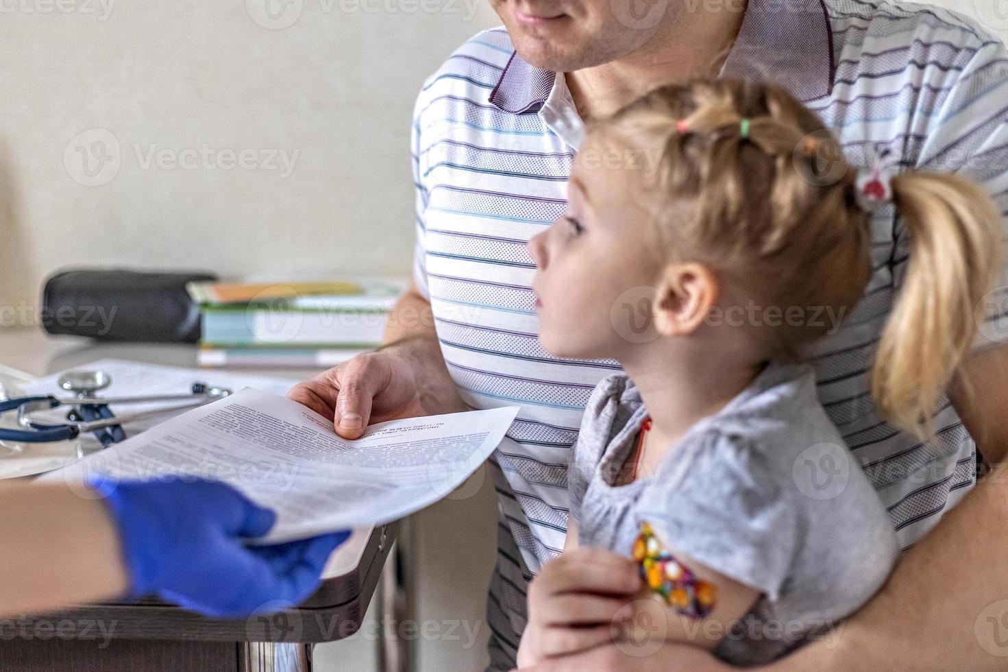 kleines Mädchen mit ihrem Vater in der Arztpraxis der Klinik. gegen Coronavirus geimpft. Der Arzt übergibt die Unterlagen an den Vater des Mädchens. das Konzept der Impfung von Covid-19 foto