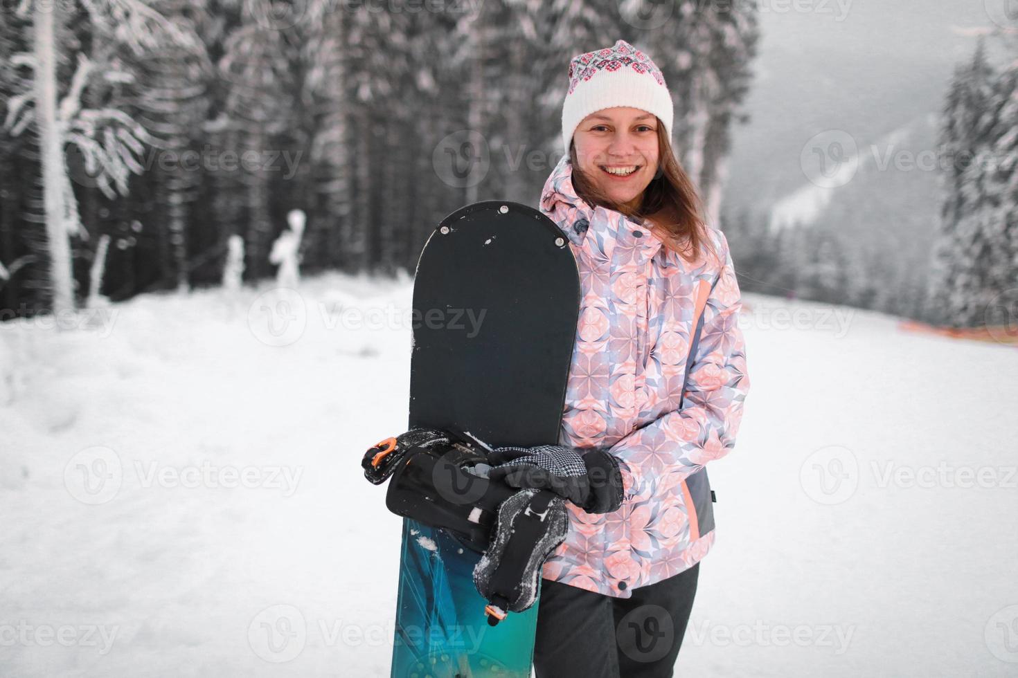 glücklich lächelnde junge Frau mit Snowboarden auf dem Berg im Winter foto