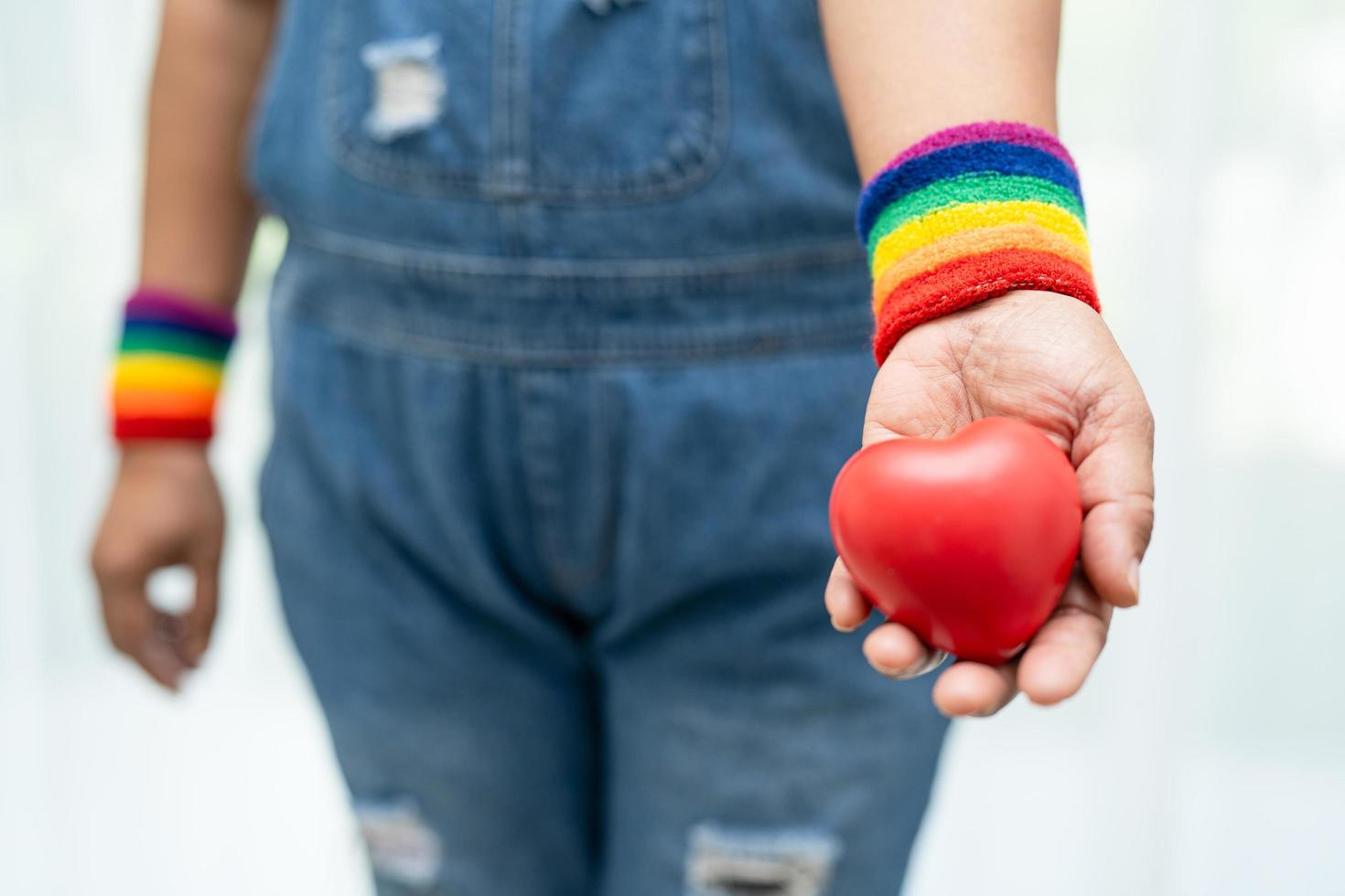 asiatische dame, die regenbogenflaggenarmbänder trägt und rotes herz hält, symbol des lgbt-stolzmonats, feiert jährlich im juni sozial für schwule, lesbische, bisexuelle, transgender, menschenrechte. foto