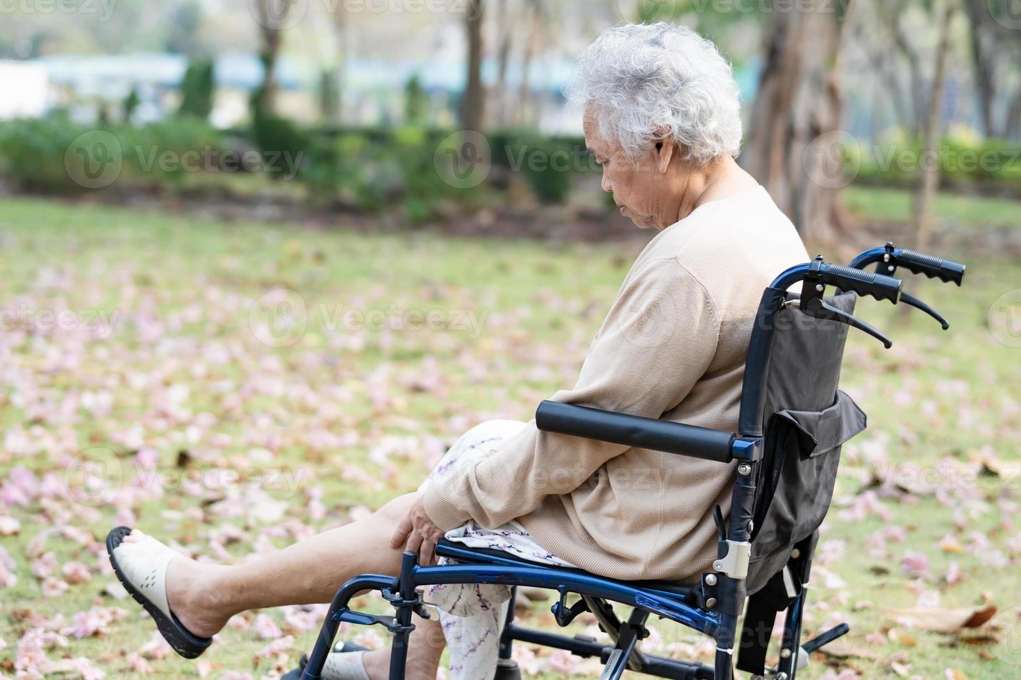 asiatische senior oder ältere alte damenpatientin schmerzt ihr knie im rollstuhl im park, gesundes starkes medizinisches konzept. foto