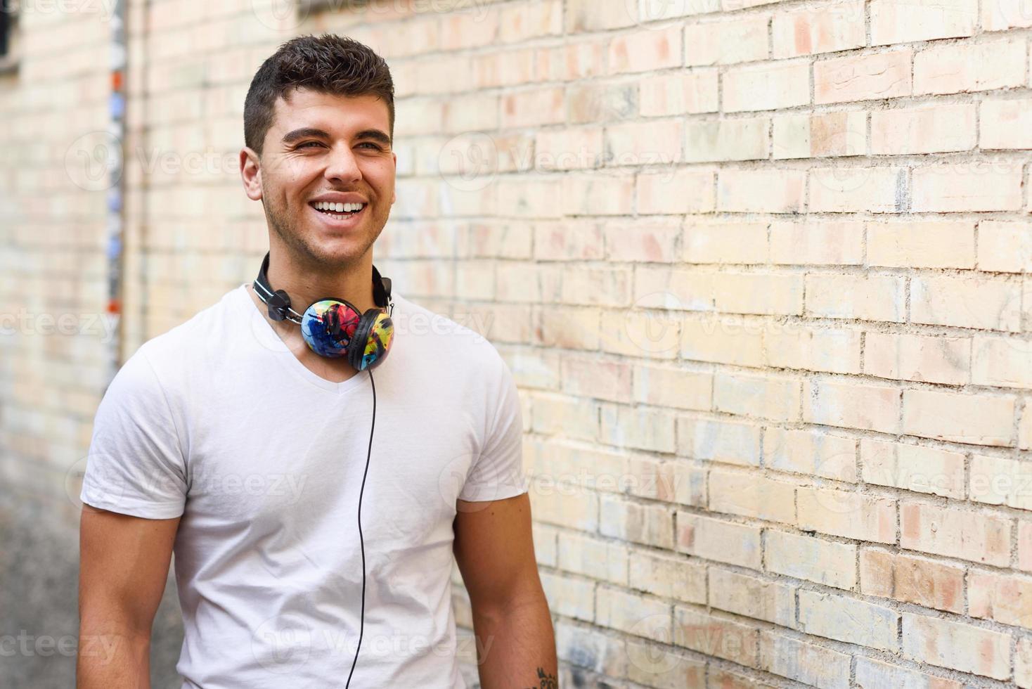 junger Mann im städtischen Hintergrund, der mit Kopfhörern Musik hört foto