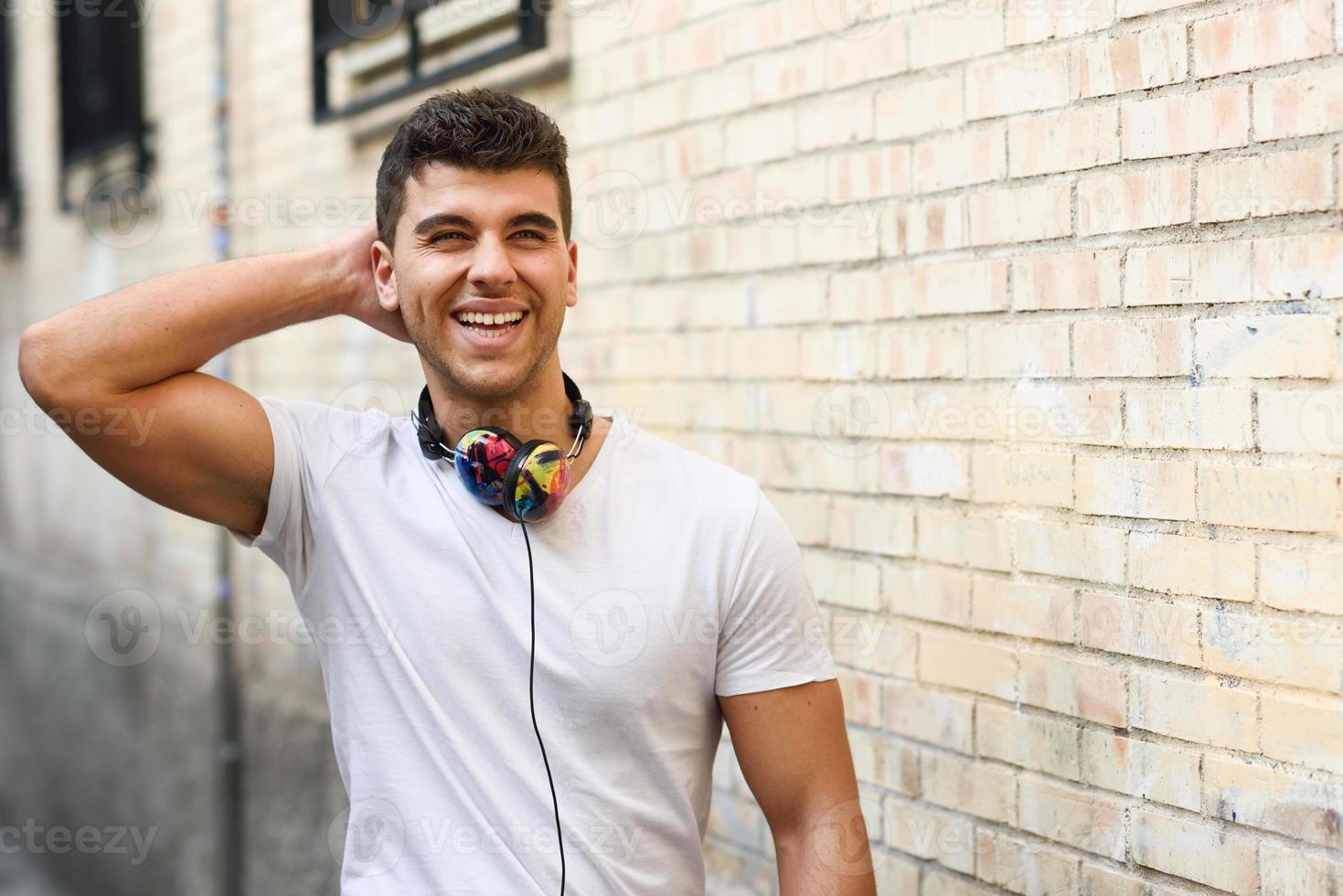 junger Mann im städtischen Hintergrund, der mit Kopfhörern Musik hört foto