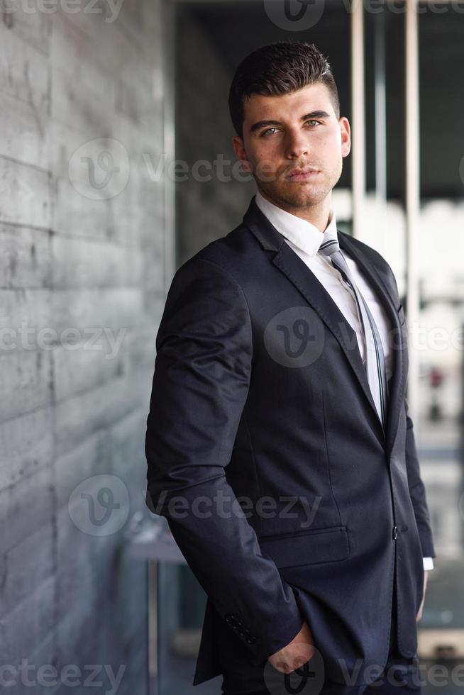 junger Geschäftsmann in der Nähe eines Bürogebäudes im schwarzen Anzug foto