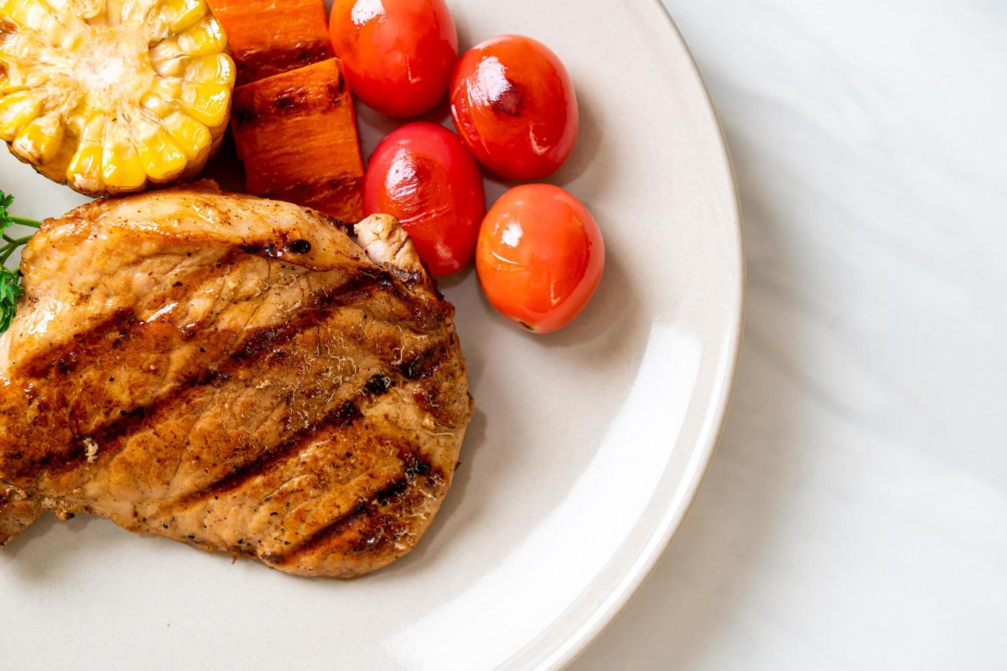 gegrilltes und gegrilltes Schweinefiletsteak mit Mais, Karotte und Tomaten foto