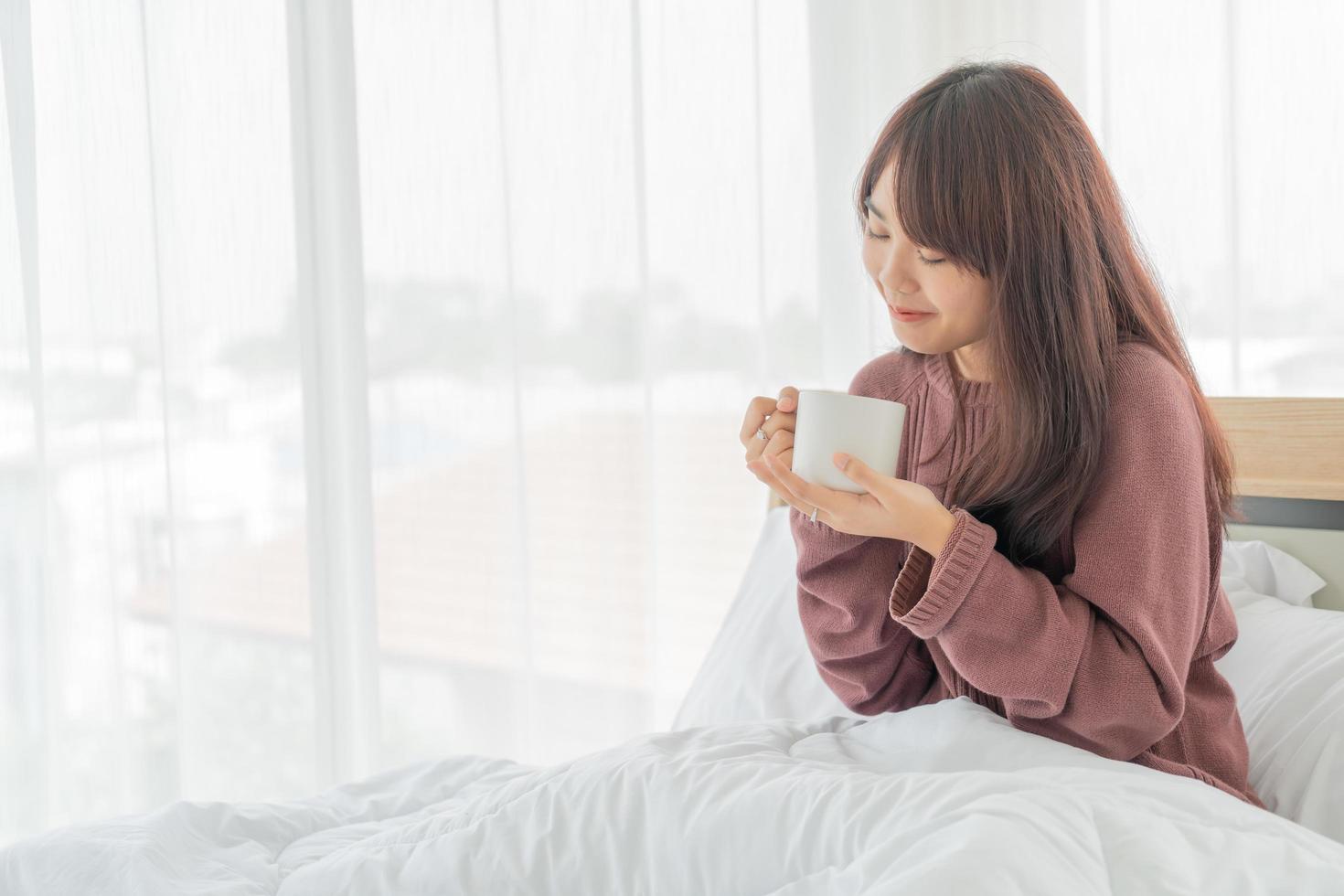 Asiatin trinkt morgens Kaffee auf dem Bett foto