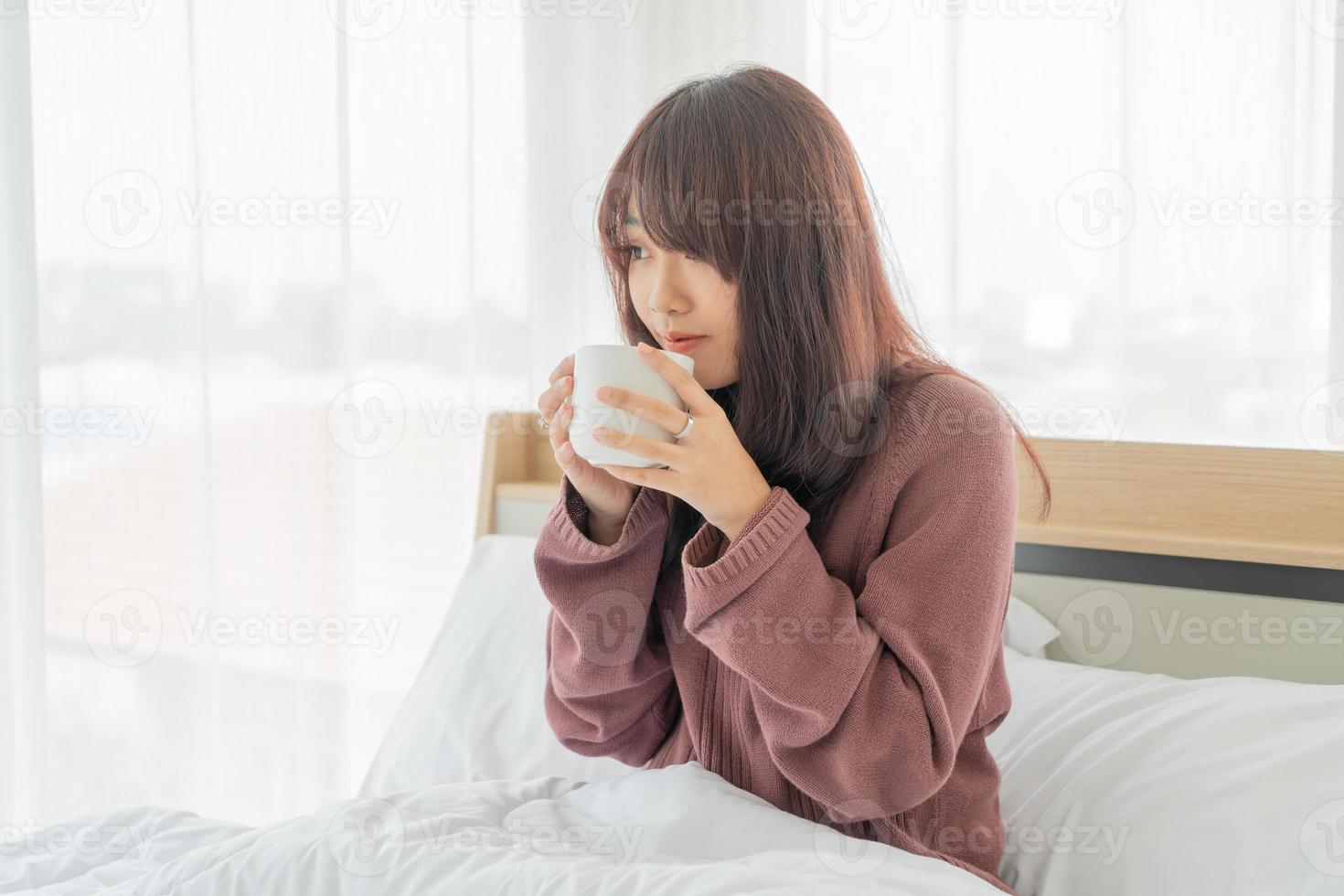 Asiatin trinkt morgens Kaffee auf dem Bett foto