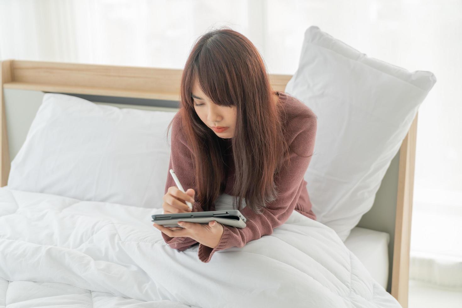 schöne asiatische frau, die mit tablette auf bett arbeitet foto