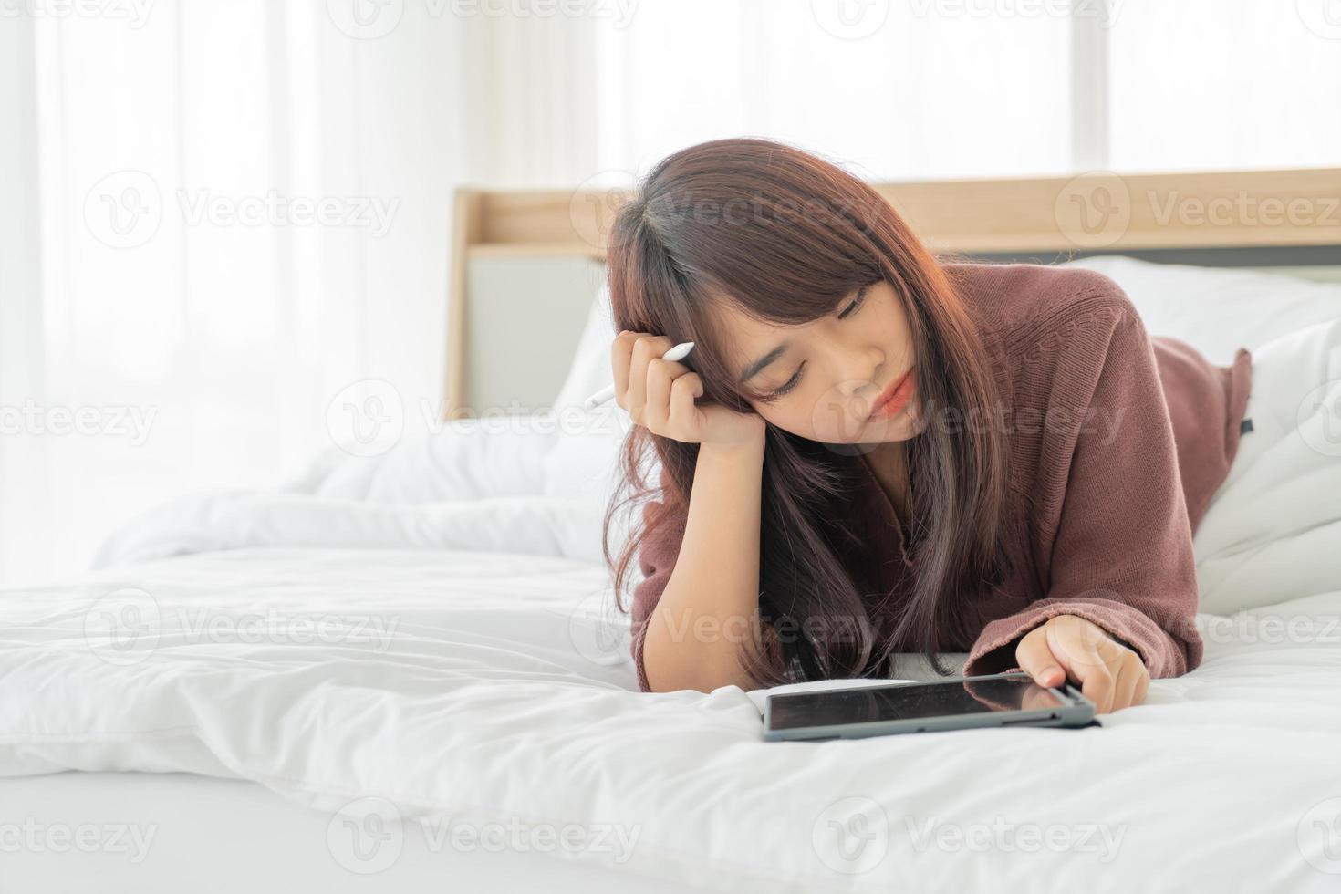 schöne asiatische frau, die mit tablette auf bett arbeitet foto