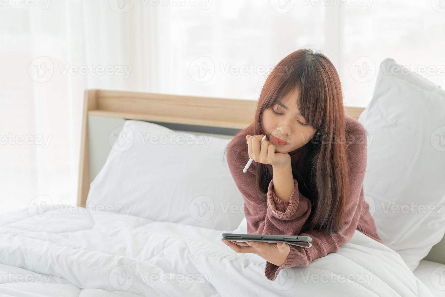 schöne asiatische frau, die mit tablette auf bett arbeitet foto