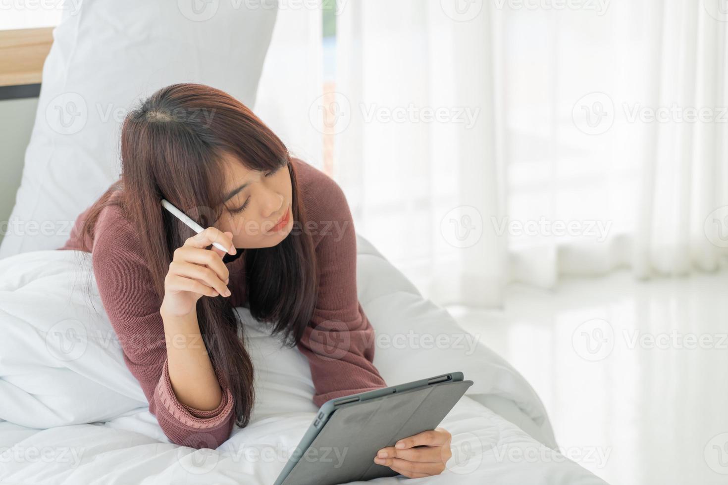 schöne asiatische frau, die mit tablette auf bett arbeitet foto