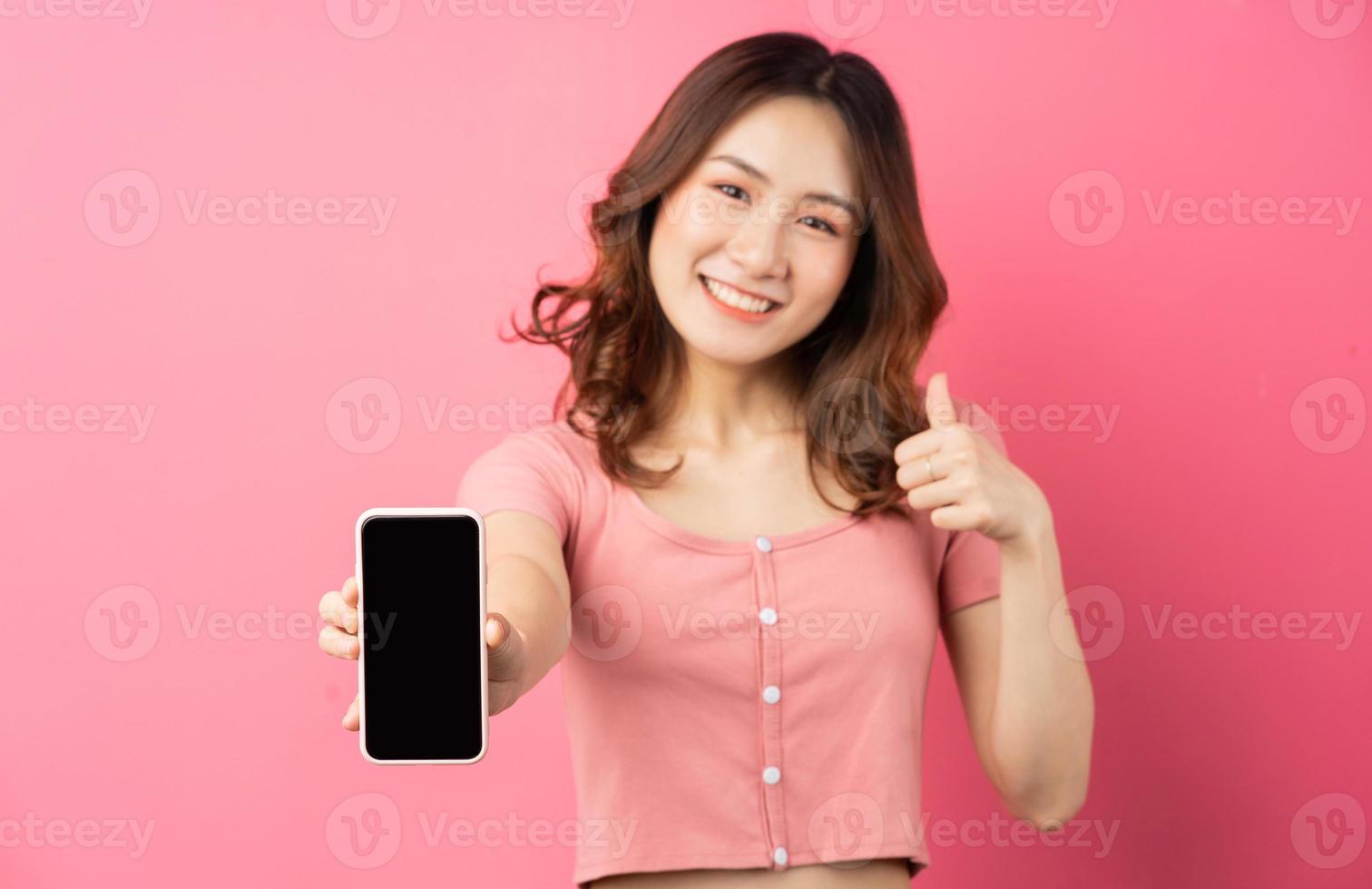 junge asiatische frau, die das telefon auf rosa hintergrund benutzt foto