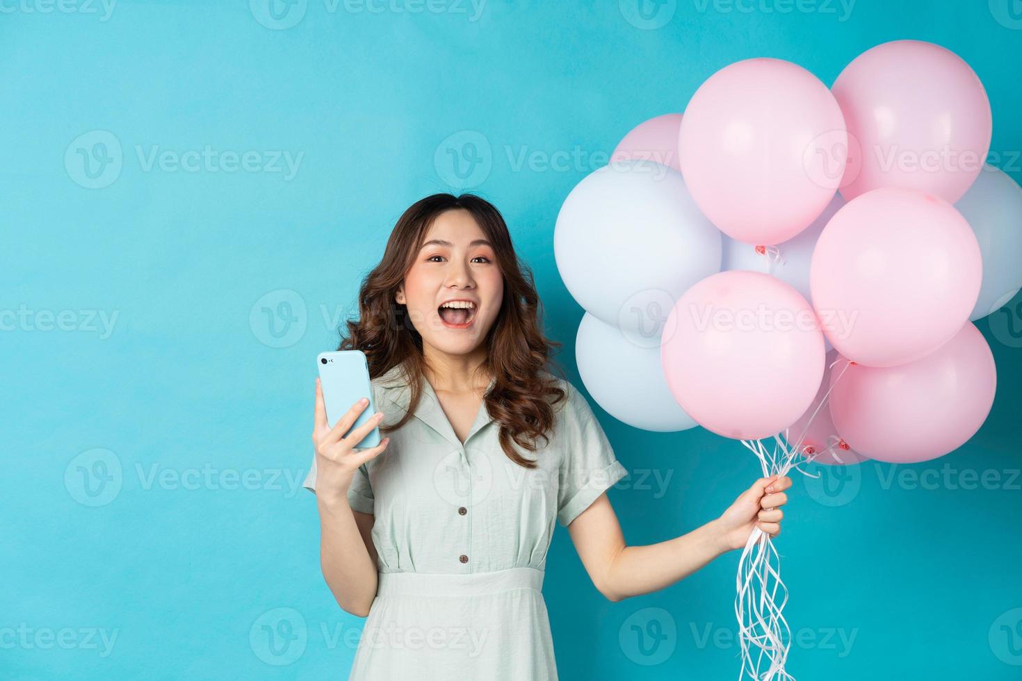 junge asiatische frau, die luftballons hält und telefon benutzt foto