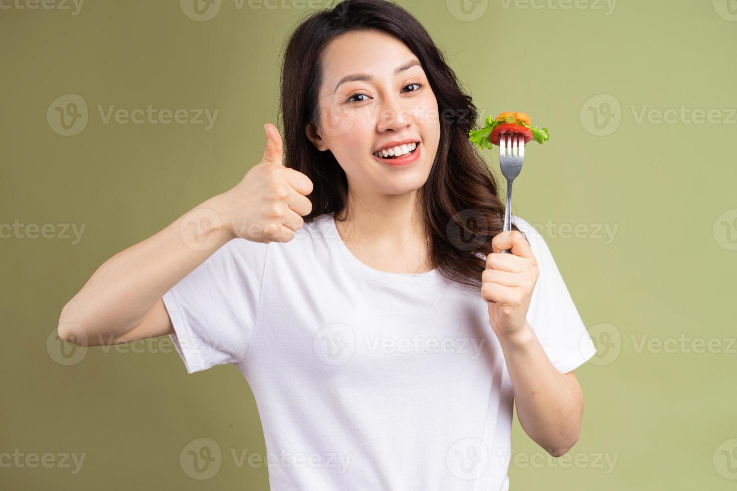 fröhliche junge asiatische Frau, die gesundes Essen im Hintergrund isst foto