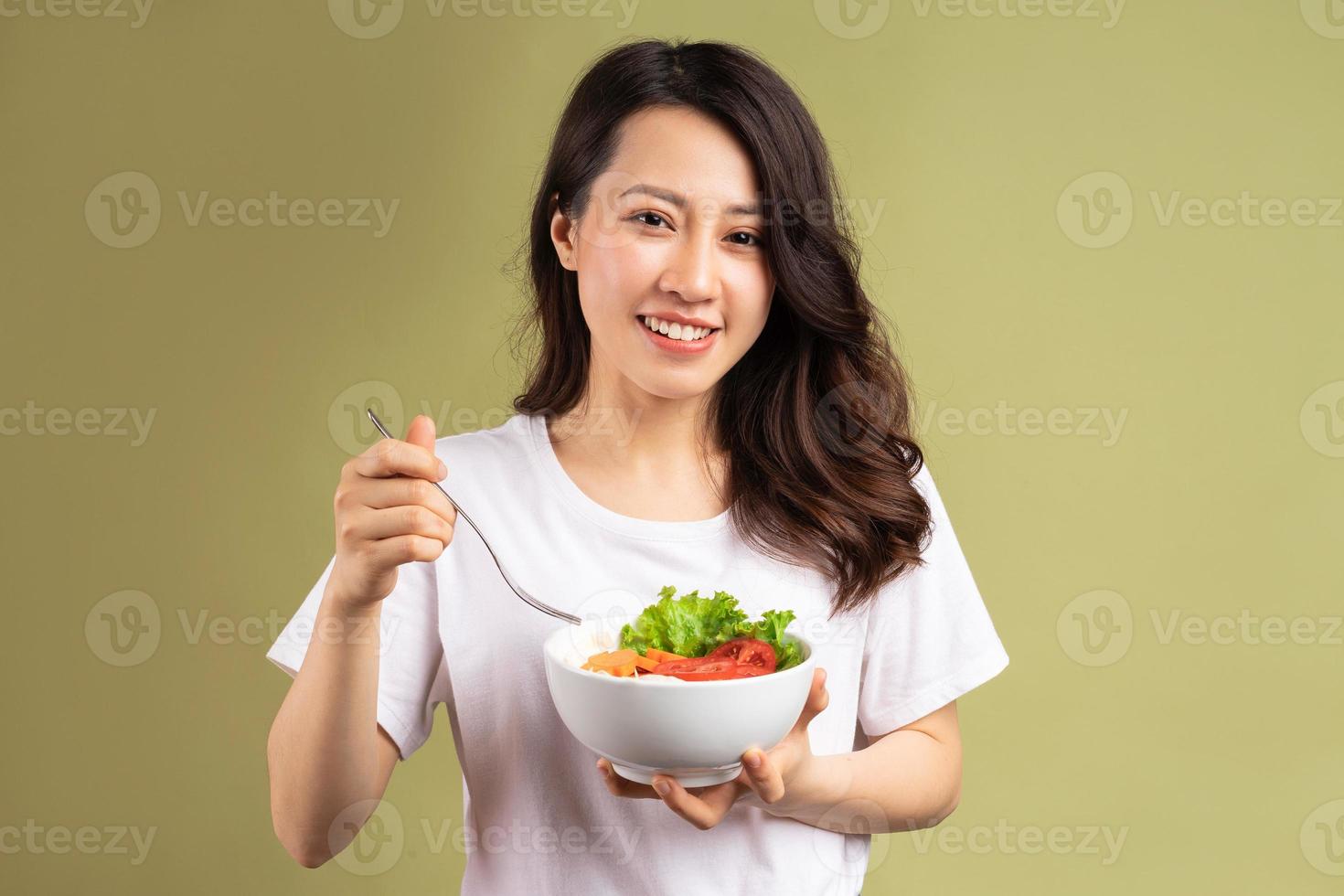 fröhliche junge asiatische Frau, die gesundes Essen im Hintergrund isst foto