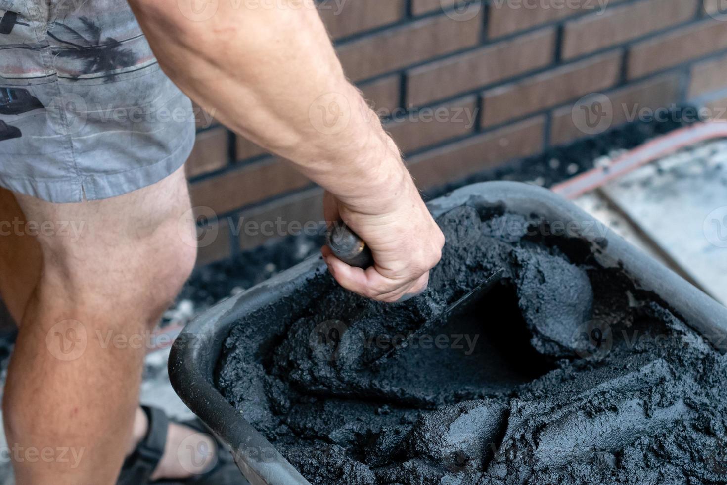 Mans Hand hält eine Kelle und gemischten Zement im Eimer. foto