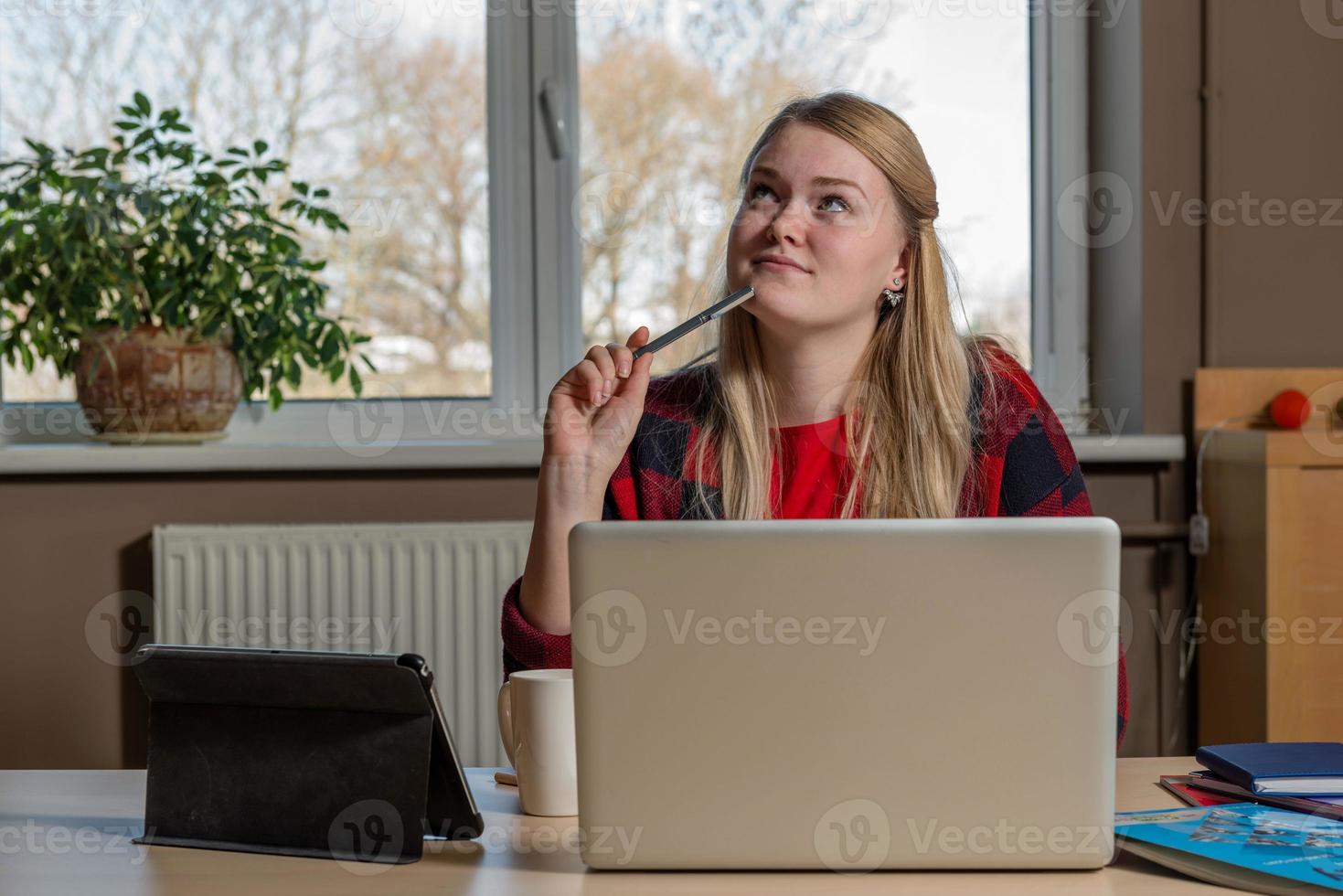 lächelnde blonde Frau sitzt an einem Laptop, trinkt Tee und arbeitet. foto