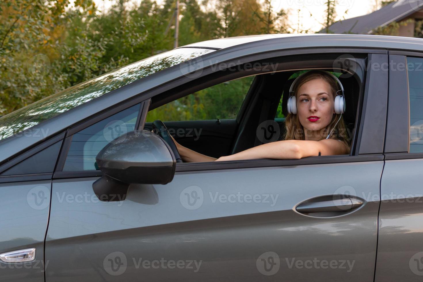 Am Steuer des Autos sitzt eine junge, schöne Frau mit langen Haaren und Kopfhörern. foto