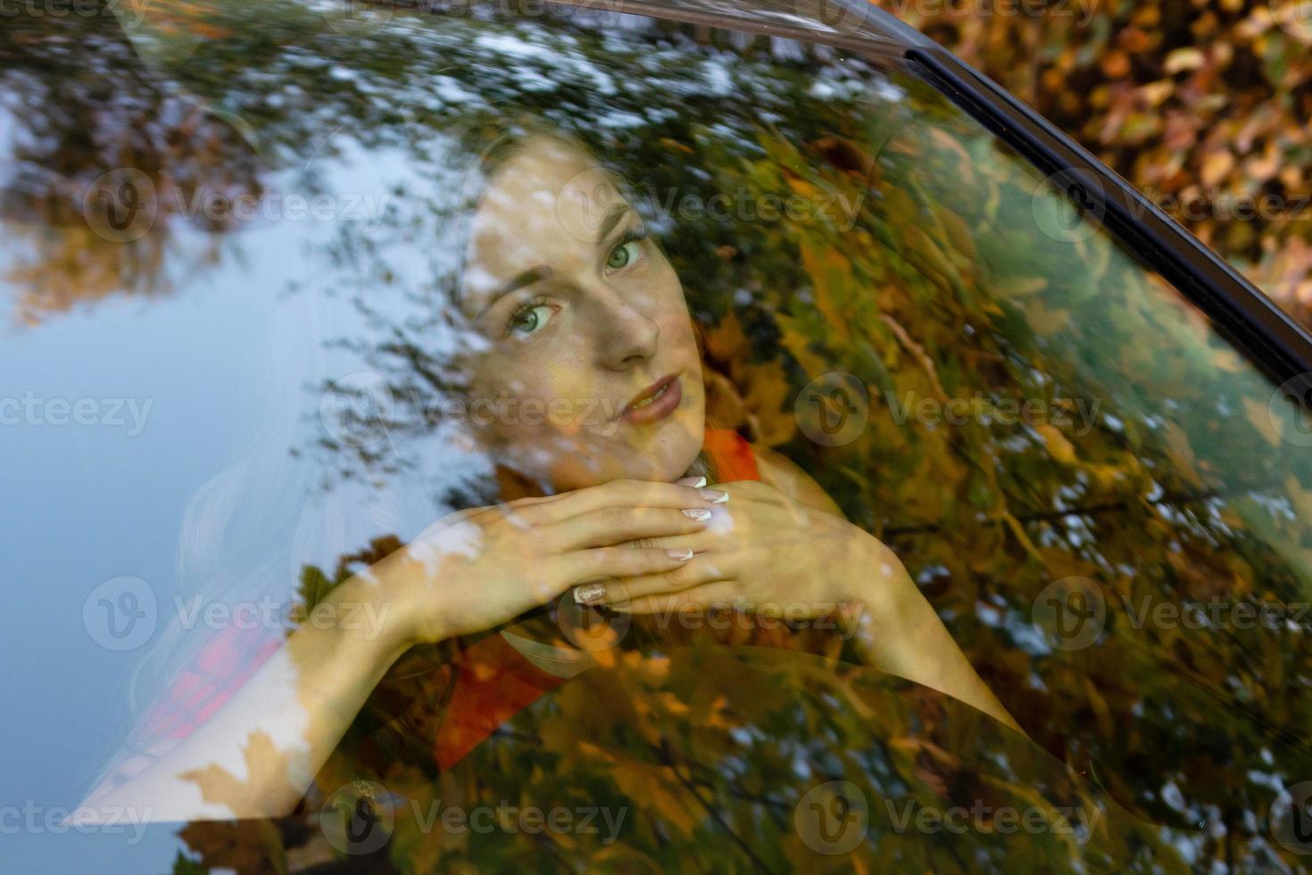 eine junge, schöne frau mit langen haaren sitzt am lenker des autos und beobachtet träumerisch durch die grelle frontscheibe. foto