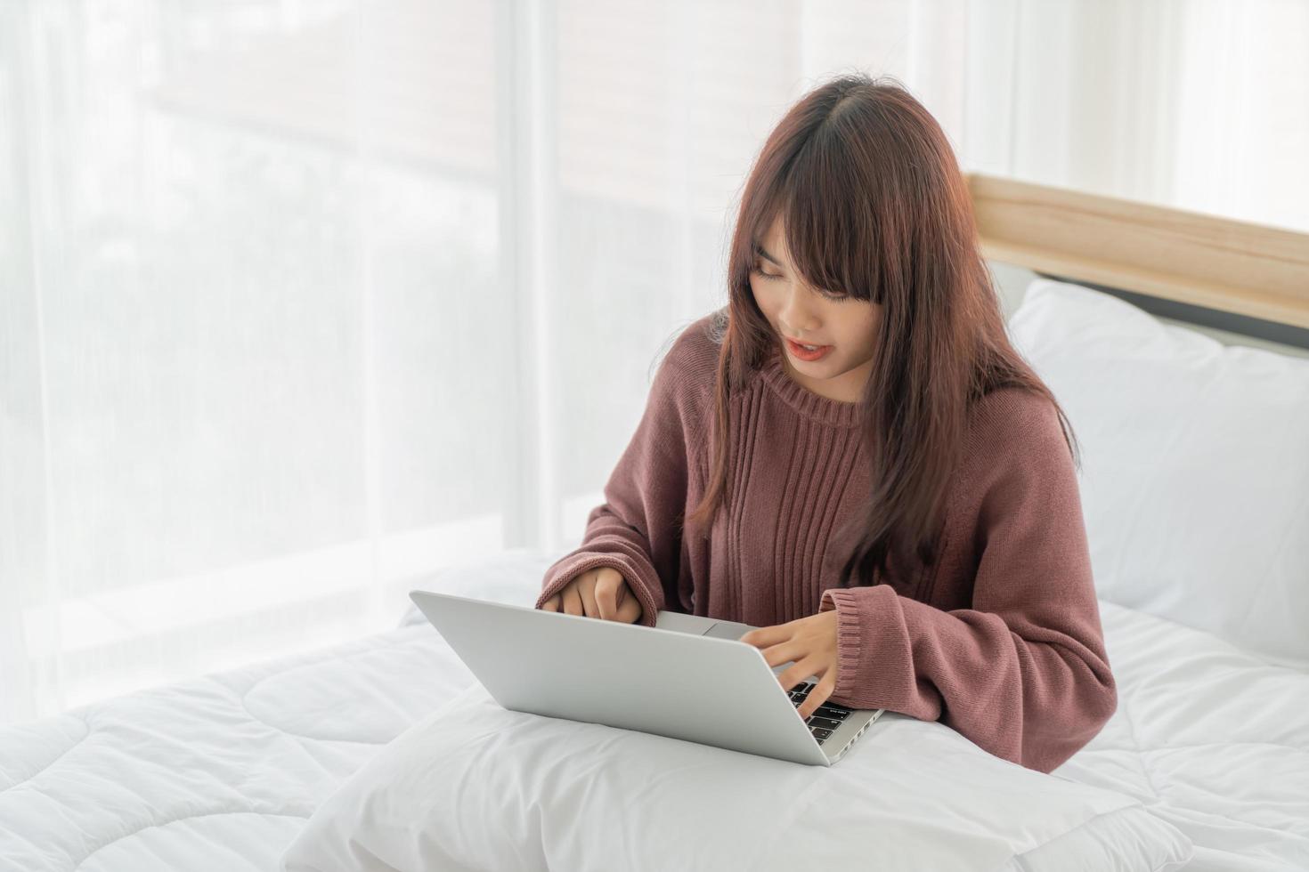 asiatische Frau, die zu Hause mit Laptop auf dem Bett arbeitet foto