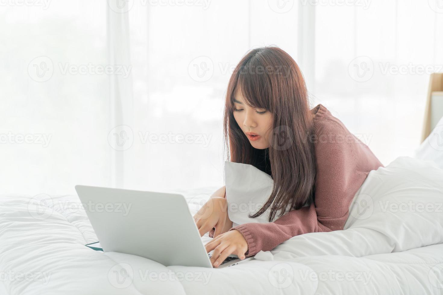 asiatische Frau, die zu Hause mit Laptop auf dem Bett arbeitet foto