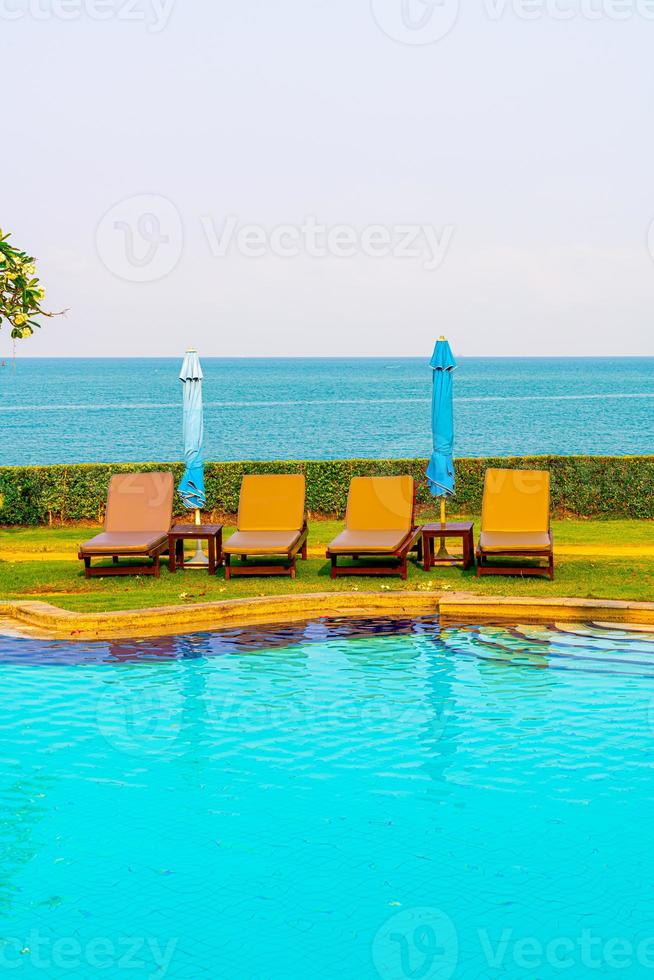 Stuhlpools oder Liegen und Sonnenschirme rund um den Pool mit Meereshintergrund - Ferien- und Urlaubskonzept foto