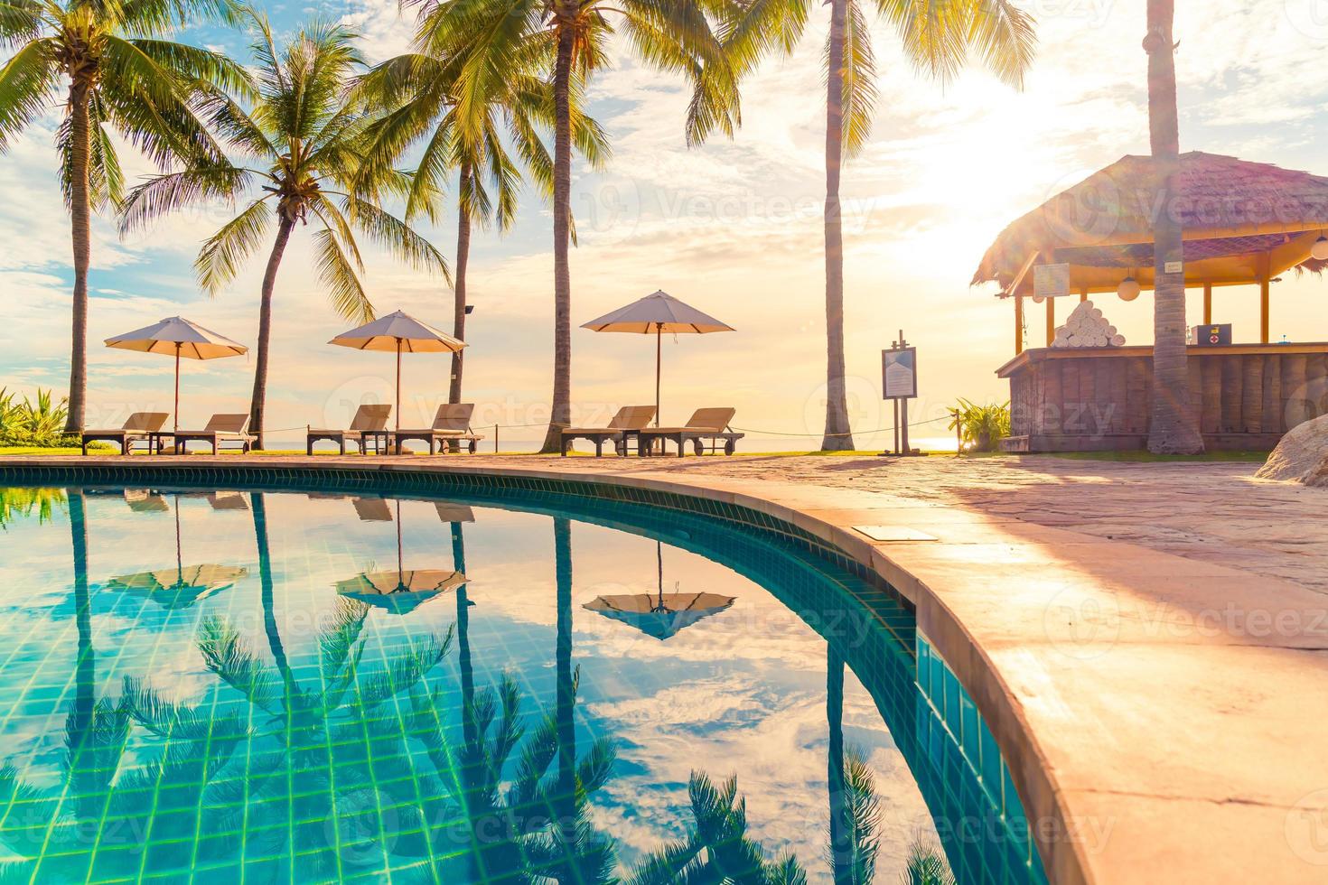 Wunderschöne Luxus-Sonnenschirme und -Stühle um einen Außenpool im Hotel und Resort mit Kokospalmen bei Sonnenuntergang oder Sonnenaufgang - Urlaubs- und Urlaubskonzept foto