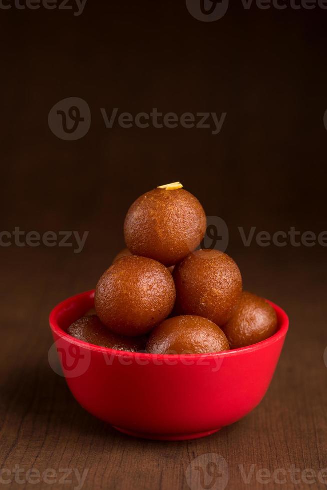 Gulab Jamun in roter Schüssel auf hölzernem Hintergrund. indisches Dessert oder süßes Gericht. foto