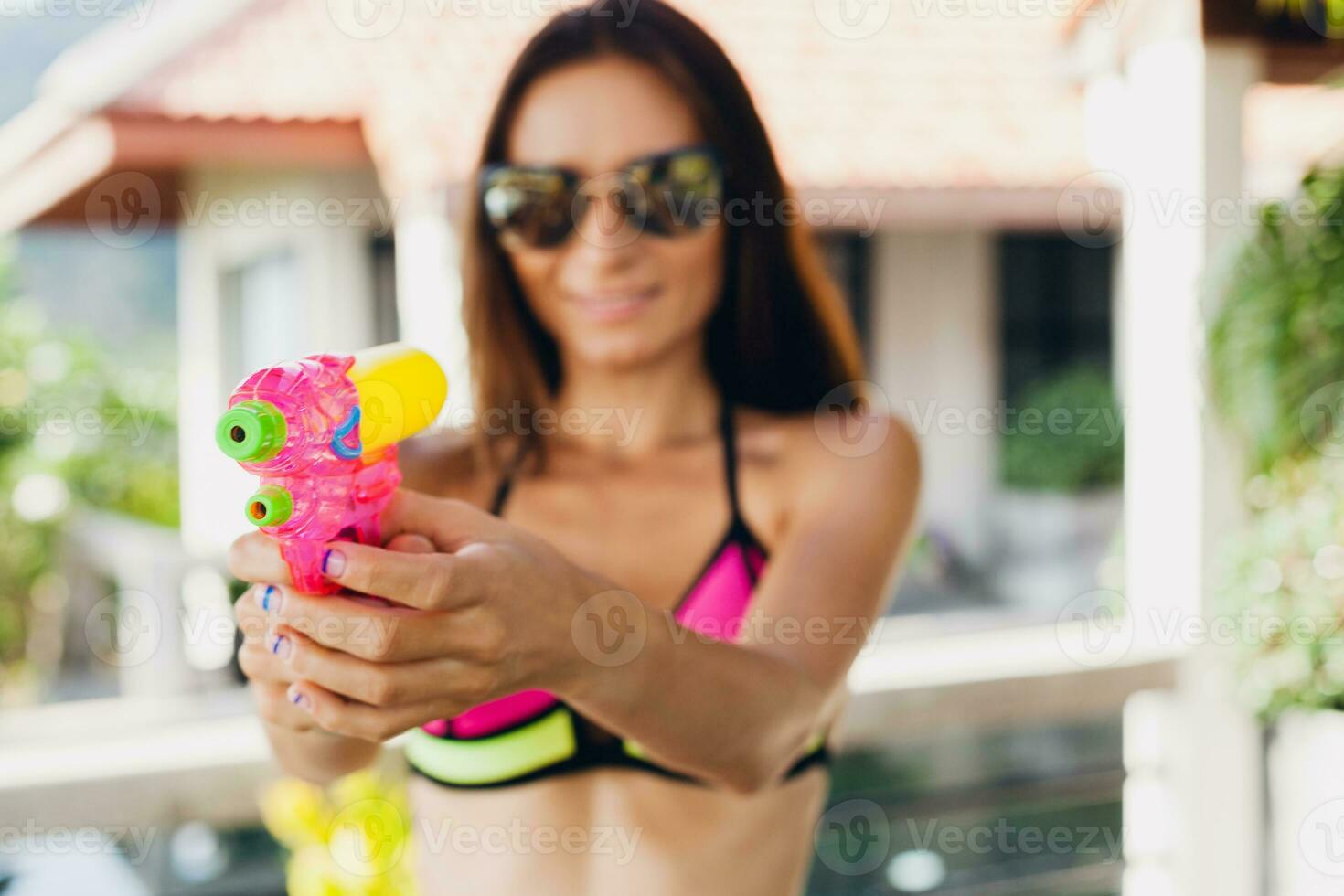 ziemlich schlank Frau spielen mit Wasserpistole Spielzeug beim Schwimmbad auf Sommer- tropisch Ferien foto