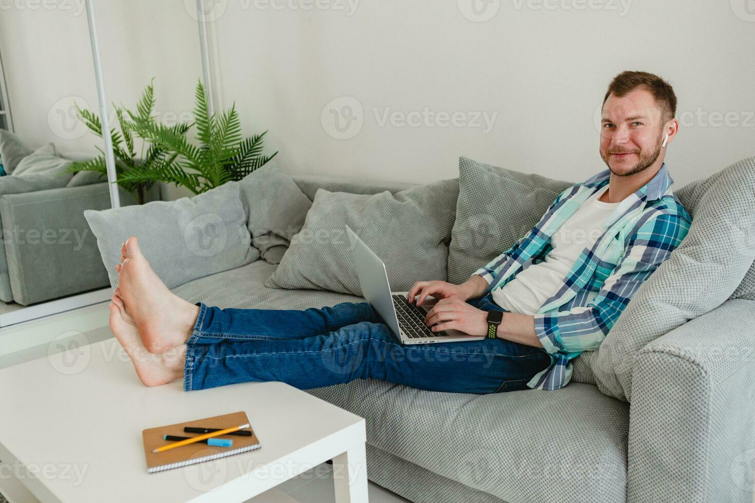 gut aussehend beschäftigt konzentriert Mann im Hemd Sitzung entspannt auf Sofa beim Zuhause beim Tabelle Arbeiten online foto