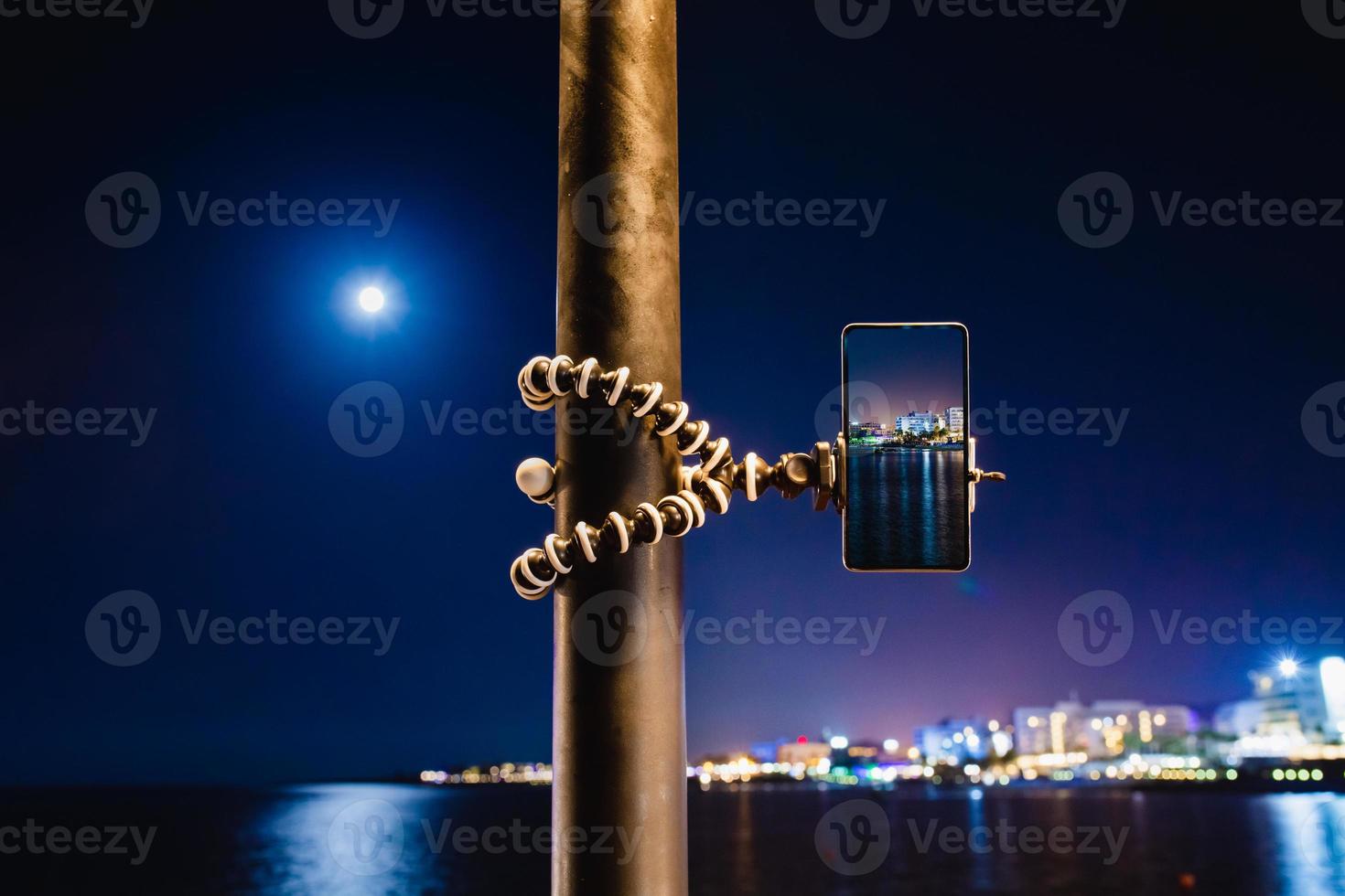 mit einem Smartphone auf einem faltbaren Stativ mit Langzeitbelichtung des Meeres bei Nacht foto