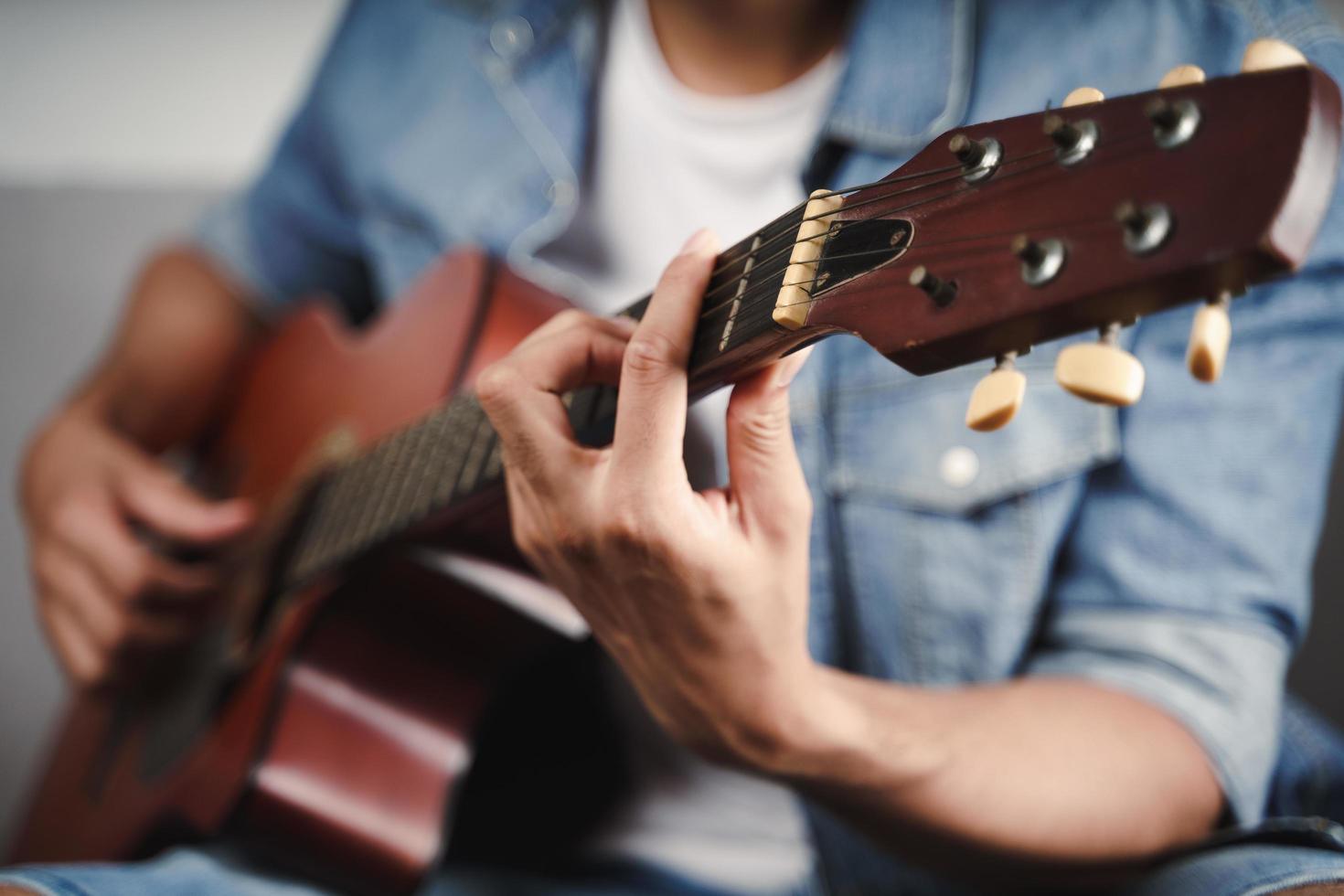 Genießen Sie einen gutaussehenden asiatischen Mann, der auf dem Sofa im Wohnzimmer Gitarre übt oder spielt foto