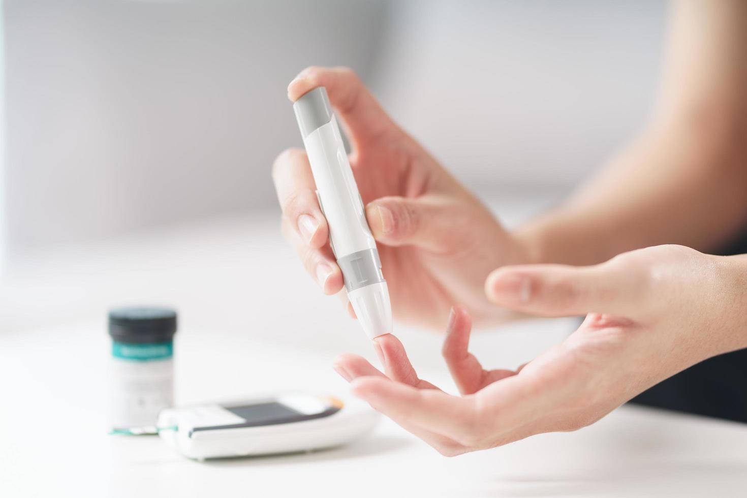 asiatische Frau mit Lanzette am Finger zur Überprüfung des Blutzuckerspiegels durch Glukosemeter, Gesundheitswesen und Medizin, Diabetes, Glykämie-Konzept foto