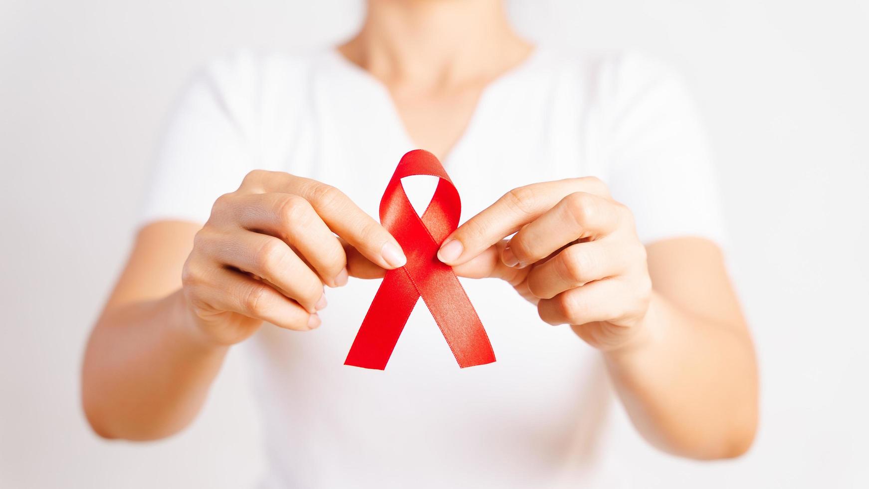 Nahaufnahmefrauenhand, die rotes Band hiv, Welt-Aids-Tagesbewusstseinsband hält. Gesundheits- und Medizinkonzept. foto