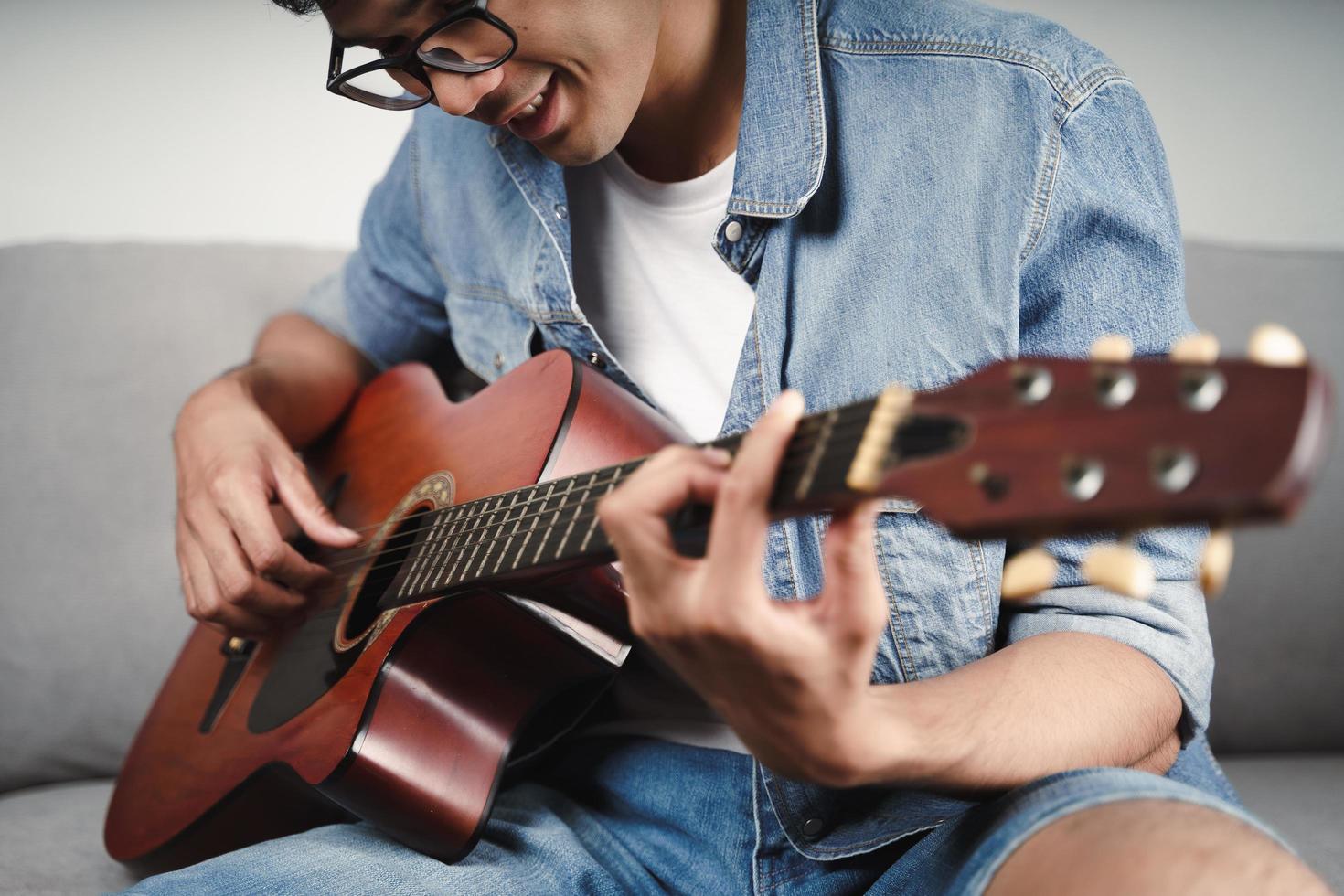 Genießen Sie einen gutaussehenden asiatischen Mann, der auf dem Sofa im Wohnzimmer Gitarre übt oder spielt foto