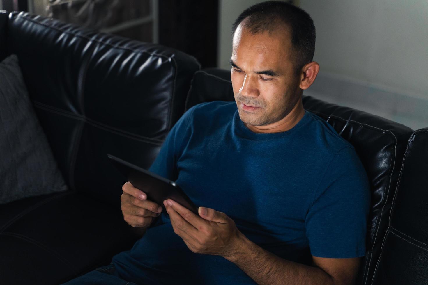 Mann sitzt auf dem Sofa, verwendet Tablet-Computer für die Arbeit oder entspannt sich zu Hause. Arbeit von zu Hause aus Konzept. foto