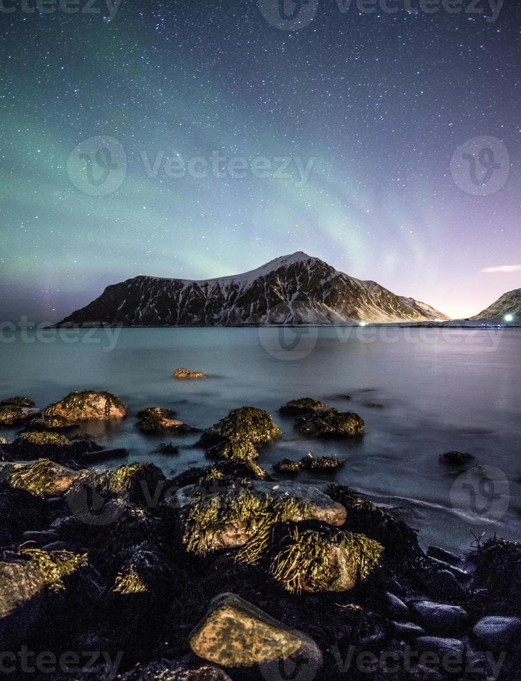 Aurora Borealis mit Sternen über Berg mit Felsen an der Küste foto