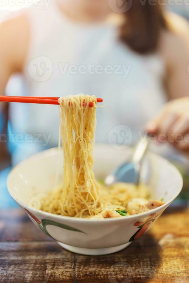 Frau Essen thailändisch Boot Nudel verdicken Suppe mit Schweinefleisch, Bälle, knusprig gebraten Schweinefleisch Haut, Basilikum Blatt und Gemüse. traditionell und berühmt Straße Essen im Thailand foto