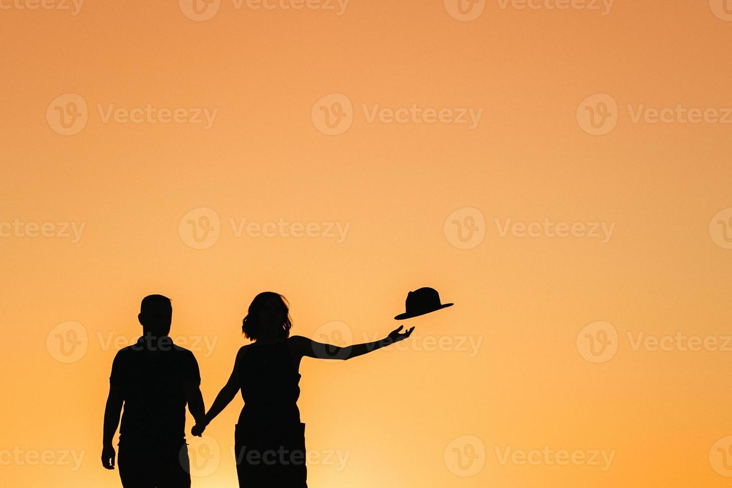 Silhouetten eines glücklichen jungen Paares auf einem Hintergrund des orangefarbenen Sonnenuntergangs in der Sandwüste foto