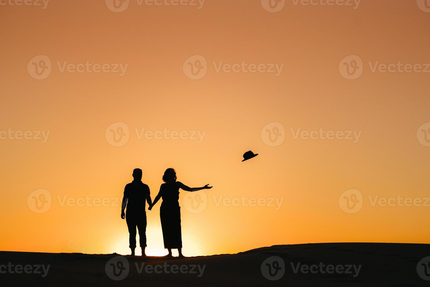 Silhouetten eines glücklichen jungen Paares auf einem Hintergrund des orangefarbenen Sonnenuntergangs in der Sandwüste foto
