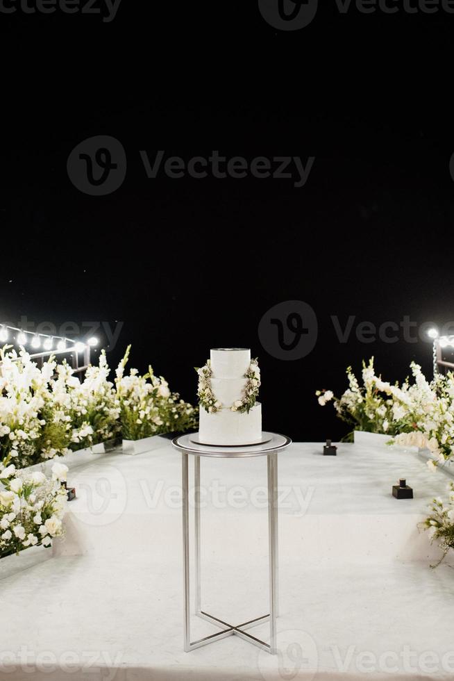 weiße Hochzeitstorte auf einem hohen Stand nahe dem weißen Podium foto