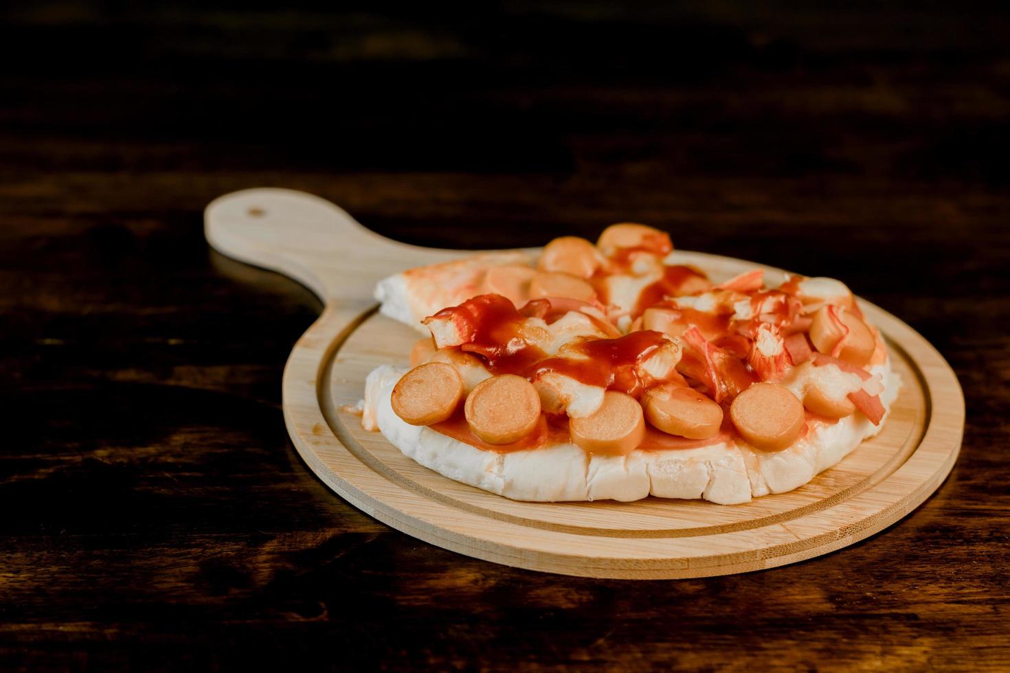Selektiver Fokus der Pizza auf einem Holztablett auf dem dunklen Holztisch foto