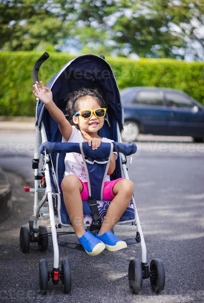 kleines Mädchen, das im Kinderwagensitz auf dem Parkplatz lächelt foto