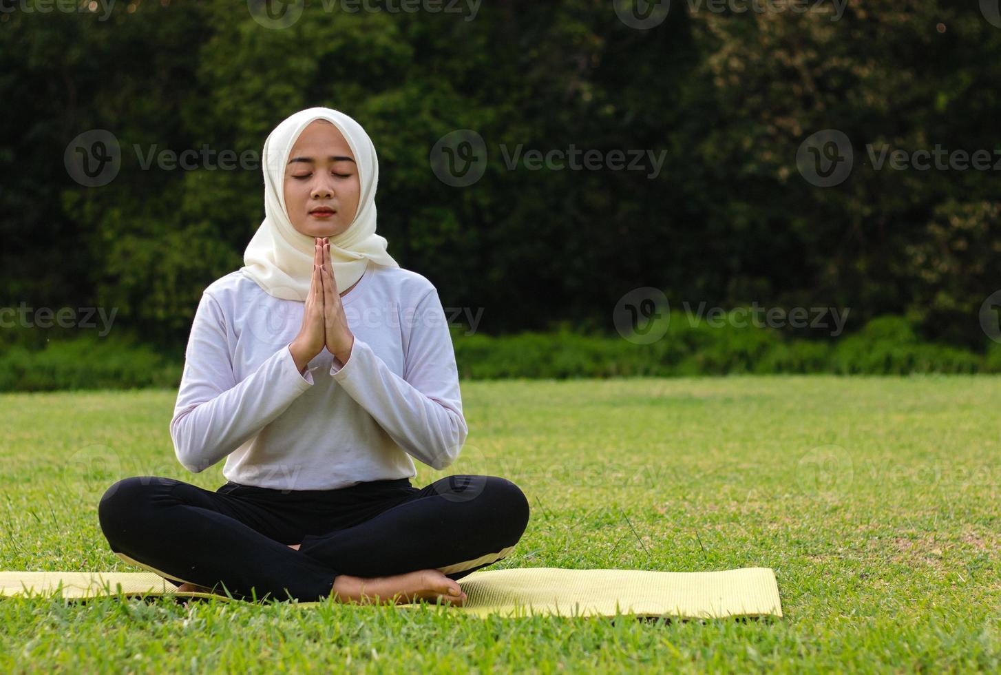 junge asiatische muslimische Frau sitzt auf dem Gras und genießt Meditation foto