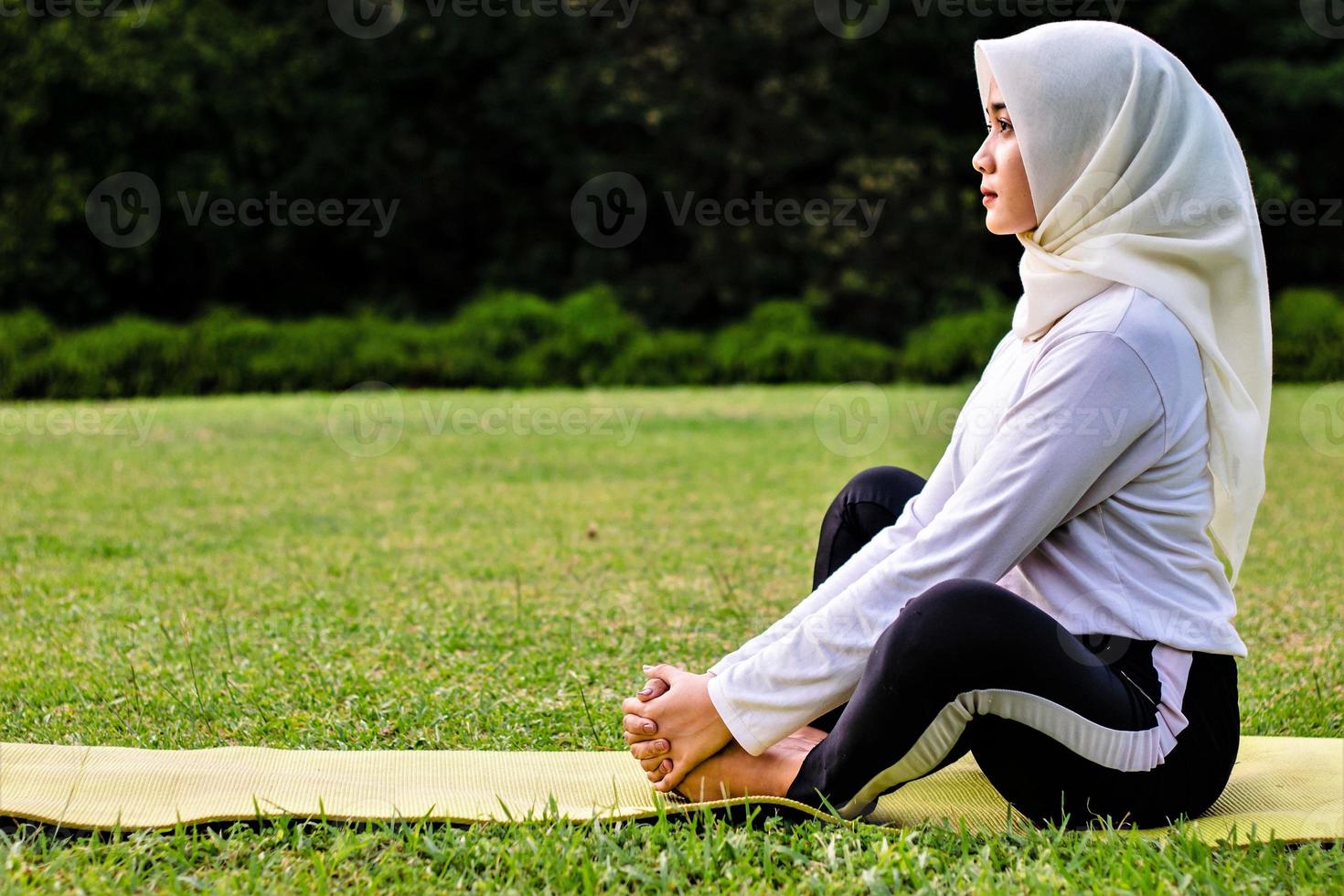 Junge muslimische Frau macht Muskeldehnung, bevor sie Yoga-Bewegungen macht foto