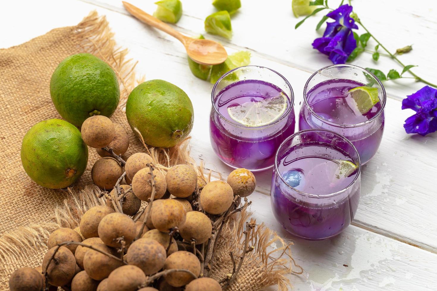 Glas Zitronensaft, Erbsenblüten und Longan auf weißem Holztisch foto