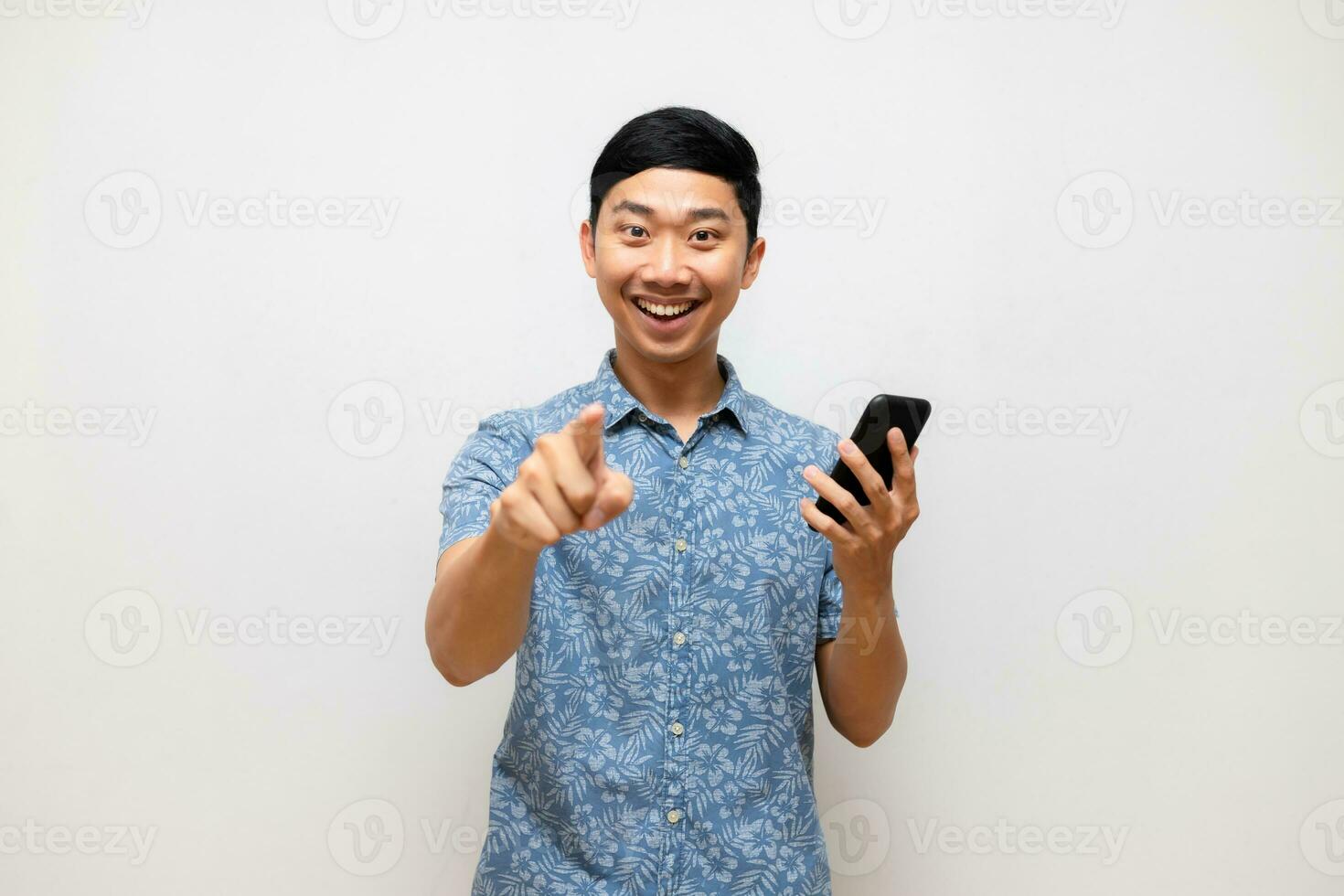 positiv asiatisch Mann Blau Hemd halten Handy, Mobiltelefon Telefon Lächeln und Punkt Finger beim Sie isoliert foto