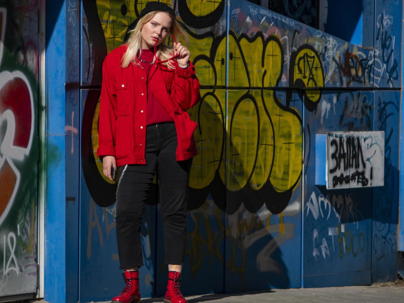 Junges Hipster-Mädchen mit Sonnenbrille in einer Strickmütze steht in der Nähe der Wand foto