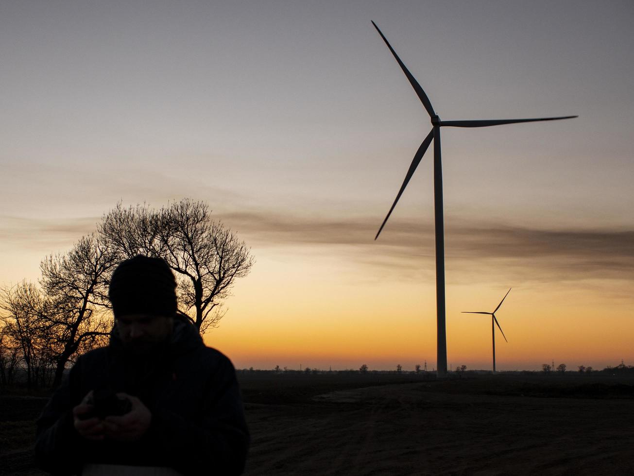 Silhouette eines Mannes bei Sonnenuntergang, der ein Foto von Windturbinen macht. Windkraftanlagen bei Sonnenuntergang